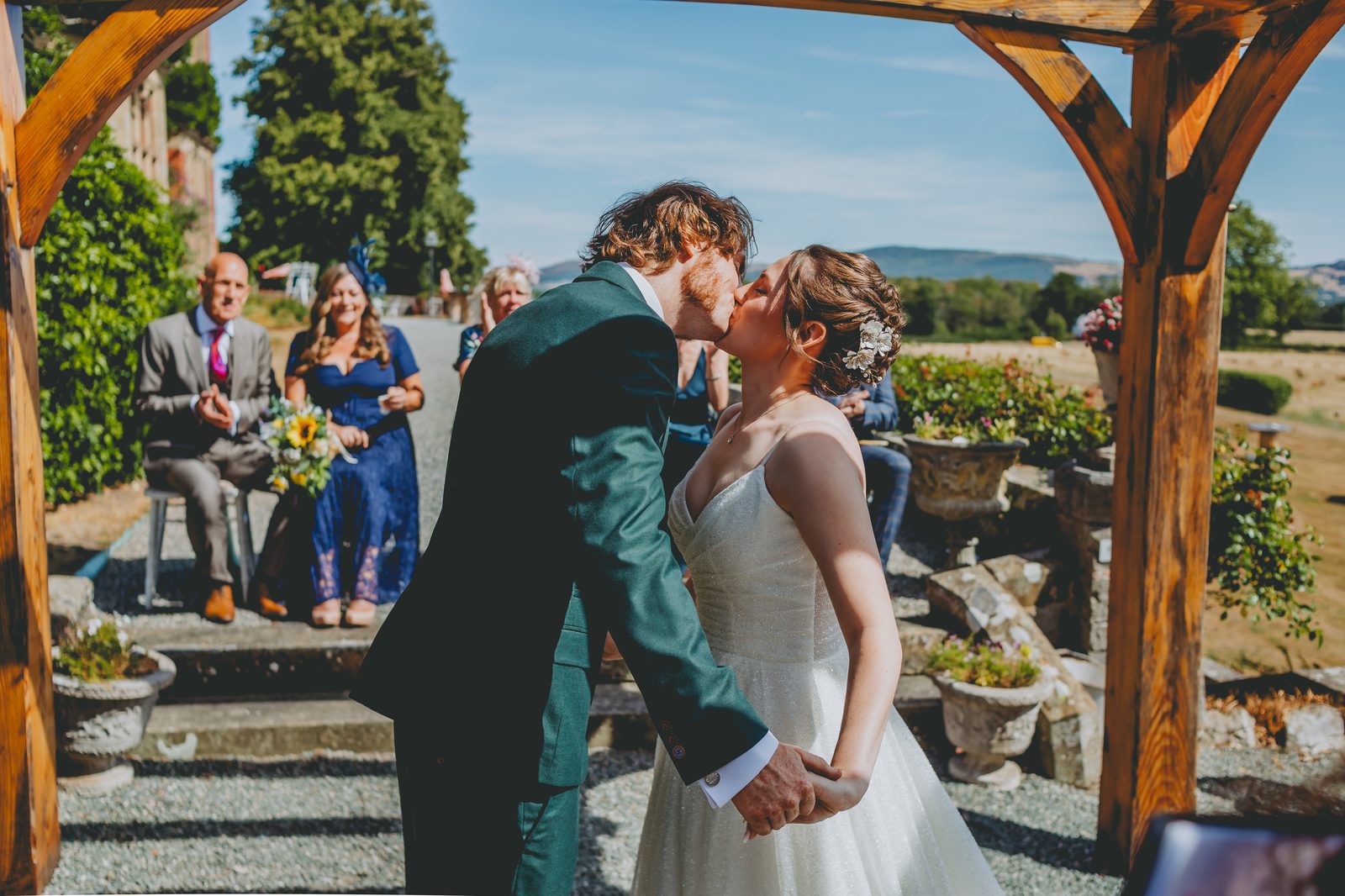 Lowri and Adam kissing under the wooden arch, Wigfair Hall wedding ceremony
