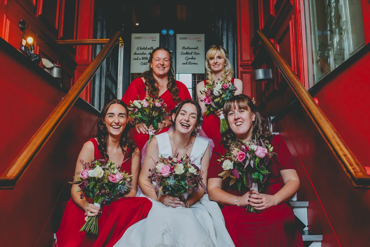 Bride, groom and bridesmaids in red on the staircase, Oddfellows Chester wedding photography